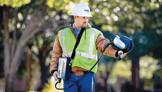Atmos worker walking and pointing a hand-held tool called a sniffer to identify natural gas leaks